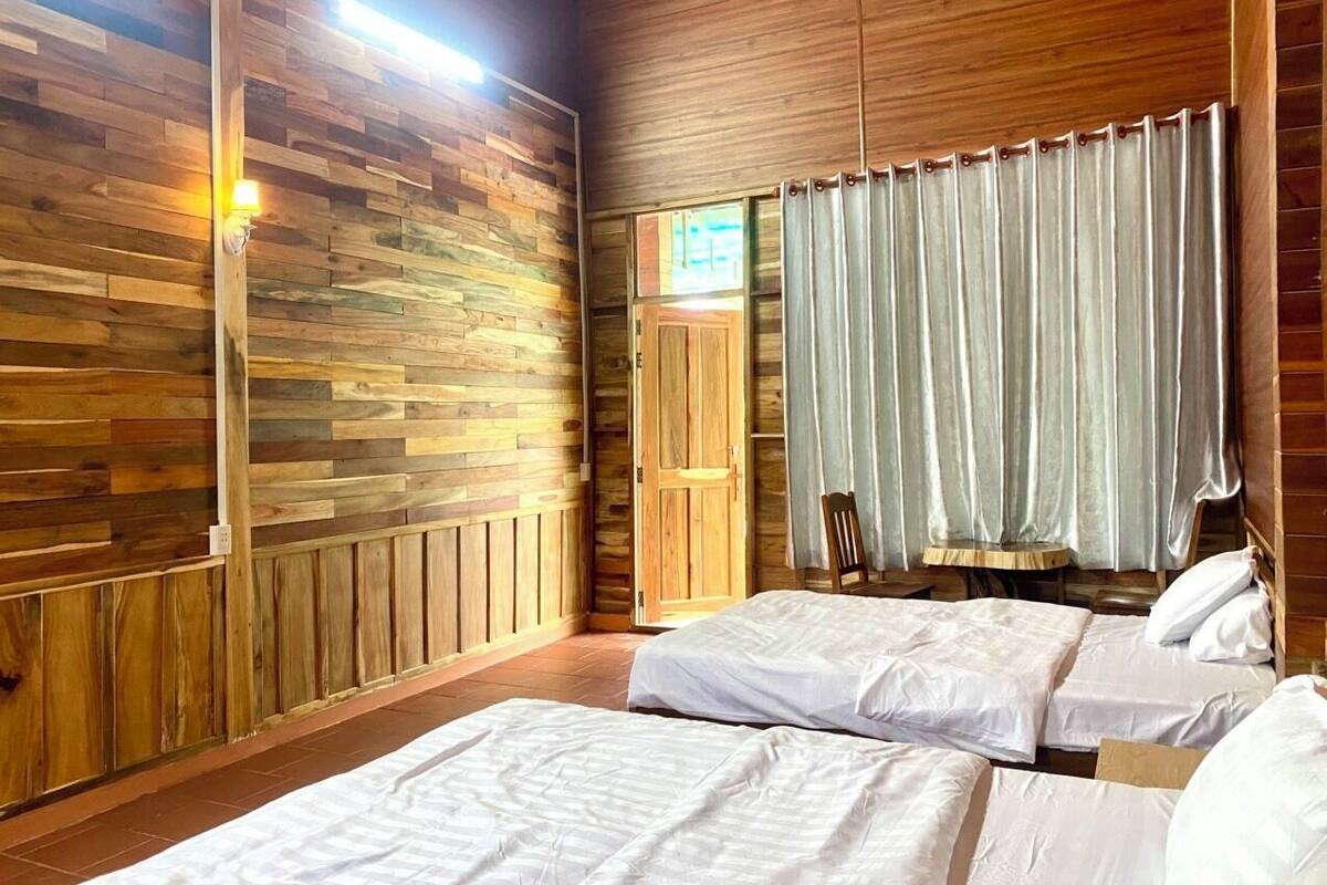 A wooden-paneled room with two beds, a wooden door, and a window with curtains.