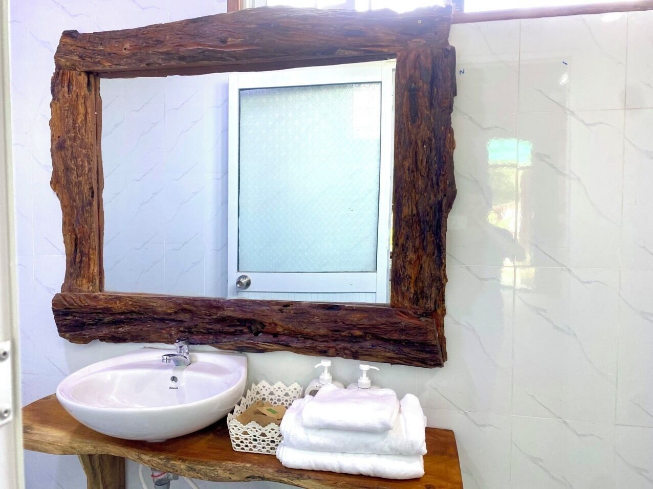 A bathroom with a rustic wooden-framed mirror, a white sink, and neatly folded towels on a wooden shelf.