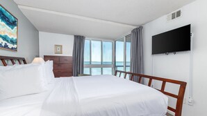A hotel room with a large bed, a dresser, a television mounted on the wall, and a window with curtains. - Sunset Sips & Sandy Trips | Your Family’s Bayfront OCMD Escape (Ocean City)