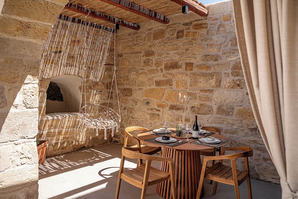 A stone-walled dining area with a round table, wooden chairs, and a hanging chair.