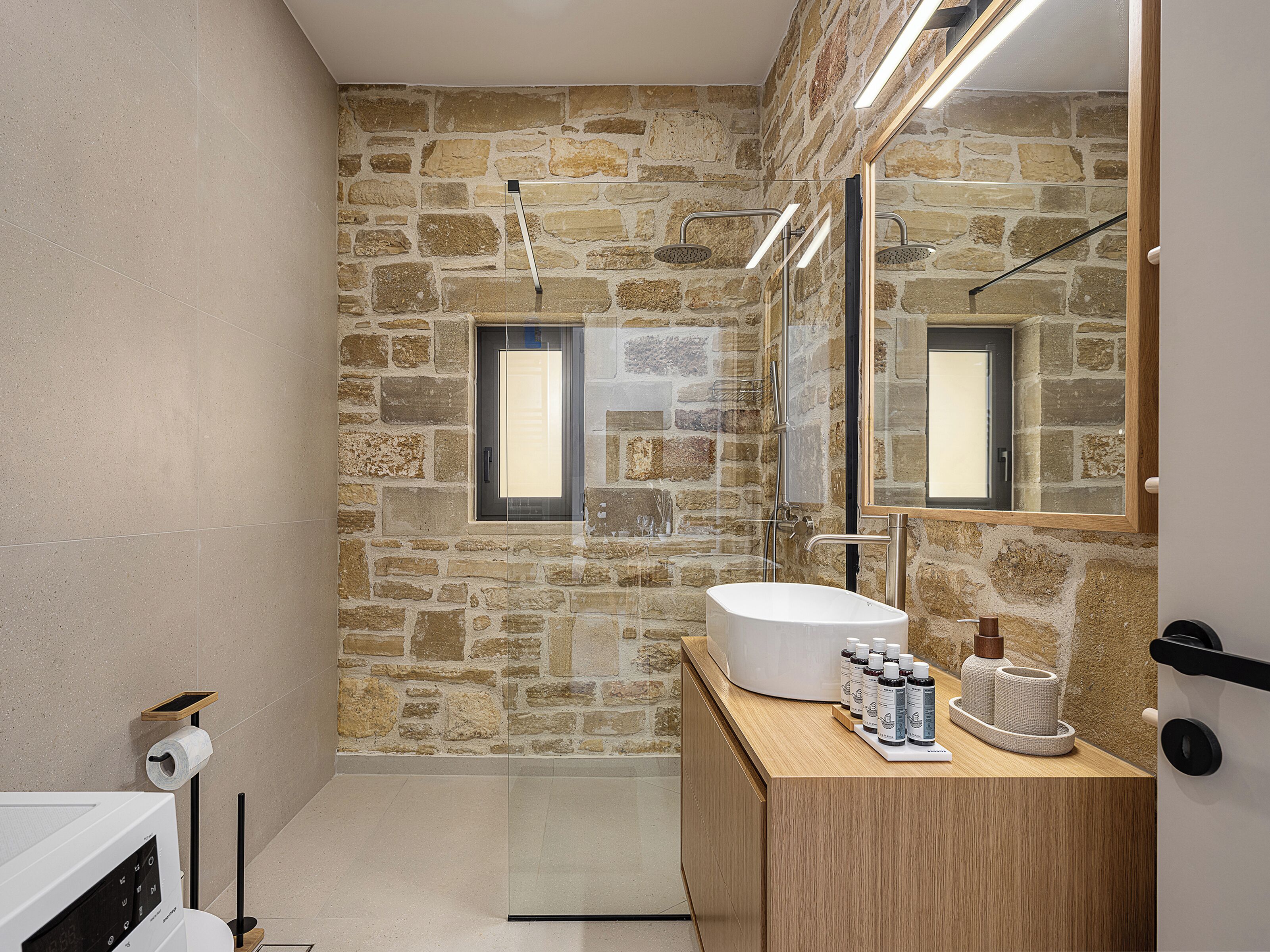 A bathroom with a stone wall, a large mirror, a wooden vanity, and a modern sink.