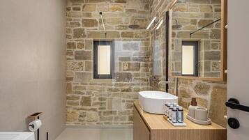 A bathroom with a stone wall, a large mirror, a wooden vanity, and a modern sink.