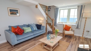 A living room with a blue sofa, wooden coffee table, and a staircase leading to an upper floor. - Puffin Cottage (Alnwick)