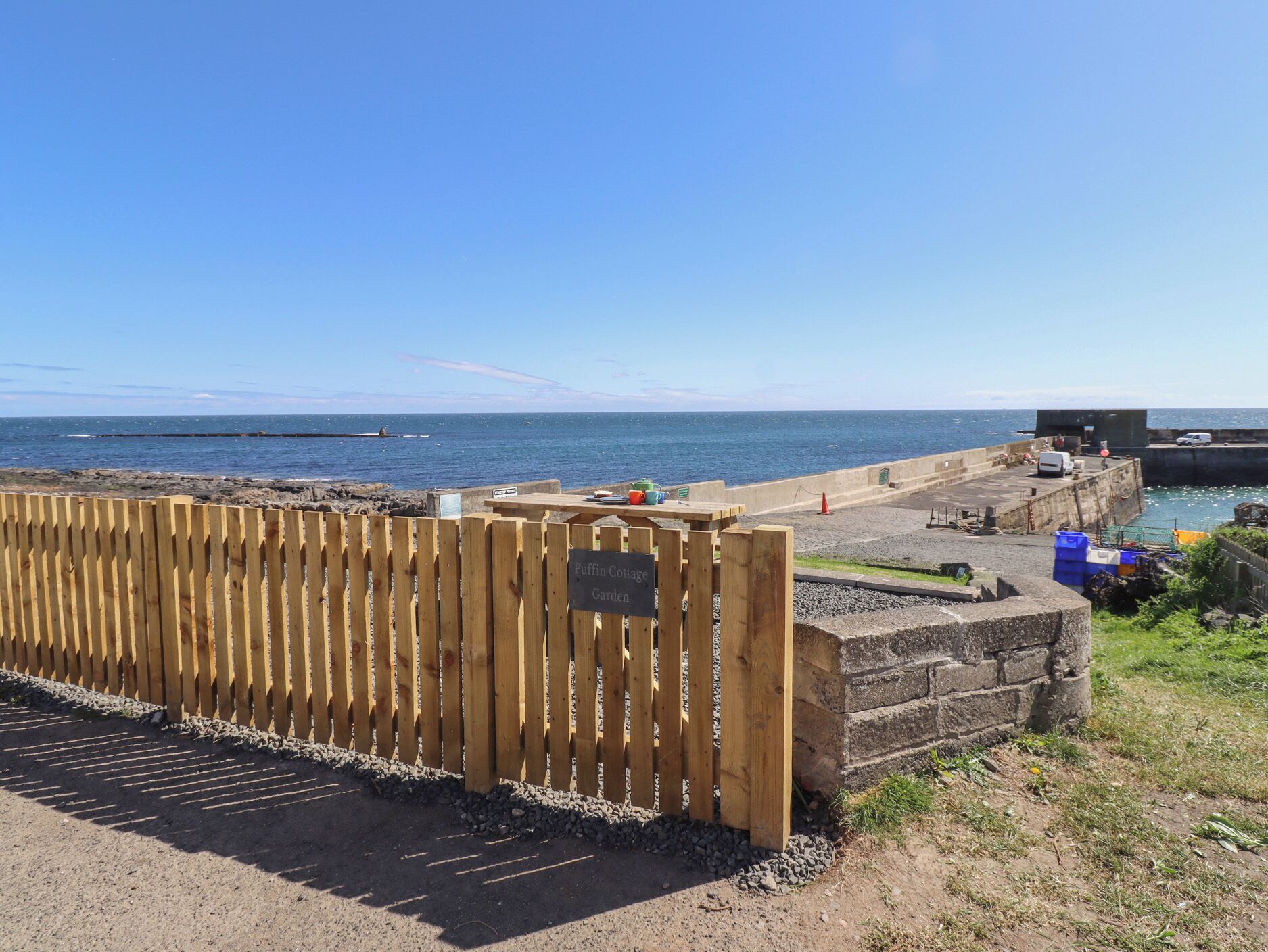 A coastal area with a wooden fence, a concrete wall, and a view of the sea.