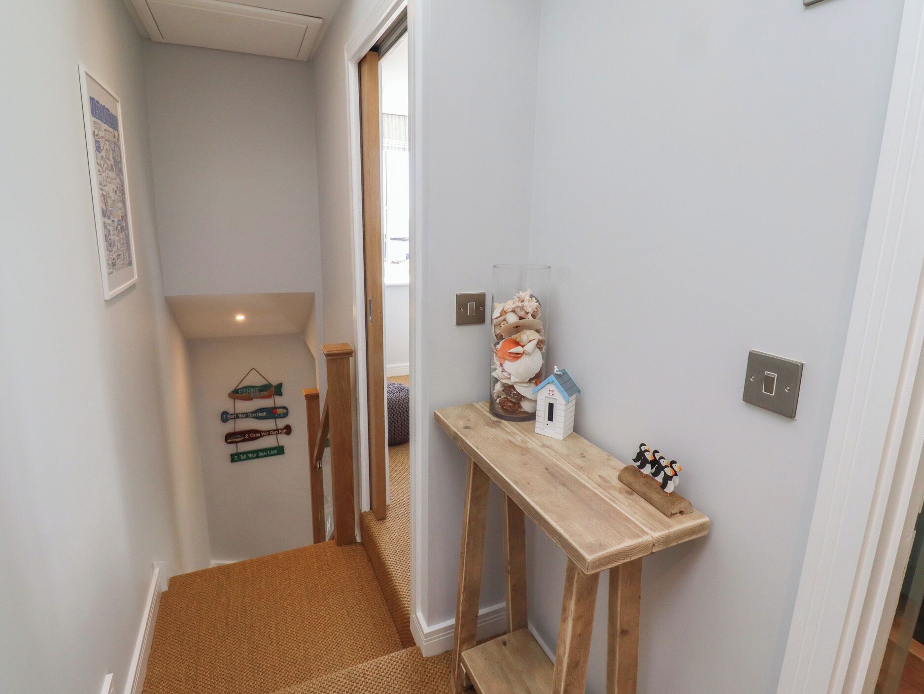 Un couloir étroit avec un banc en bois, une petite décoration représentant une maison blanche et un panneau fixé au mur.
