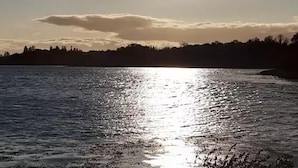 A body of water reflecting sunlight with a distant tree line silhouette. - 2 Bed Cottage-sleeps 4-private Garden-parking (Omagh)