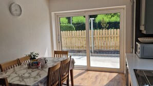 A kitchen with a marble countertop, wooden chairs, a dining table, a clock on the wall, and a sliding glass door leading to a garden. - 2 Bed Cottage-sleeps 4-private Garden-parking (Omagh)