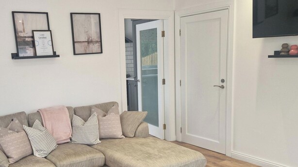 A living room with a sectional sofa, a flat-screen TV mounted above a shelf, and a door leading to a hallway. - 2 Bed Cottage-sleeps 4-private Garden-parking (Omagh)