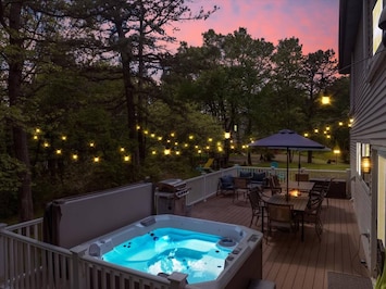 Nighttime view of the hot tub on the deck, glowing softly under warm string lights, creating a cozy and inviting atmosphere perfect for relaxing evenings.