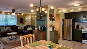 A modern kitchen with a stainless steel refrigerator, a dining area with a wooden table and chairs, and a living room with a leather sofa and a ceiling fan. - Throwback Lodge - Hot Tub - Pet Friendly (Gouldsboro)
