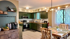 A modern kitchen with green cabinets, a stainless steel oven, and a dining area with a wooden table and chairs. - Throwback Lodge - Hot Tub - Pet Friendly (Gouldsboro)