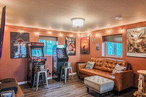 Quarto com tema retrô, com jogos de fliperama, um sofá de couro e cartazes antigos nas paredes.