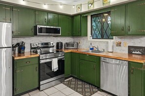 Une cuisine avec des meubles de rangement verts, des appareils électroménagers en acier inoxydable, un four à micro-ondes, un grille-pain et un évier.