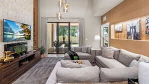 A modern living room with a flat-screen TV, wooden entertainment unit, grey sofa, and pendant lighting.