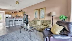 A living room with a sofa, coffee table, and a kitchen area in the background. - New For 2025! Two Bedroom Bayfront Condo On 79th St (Ocean City)
