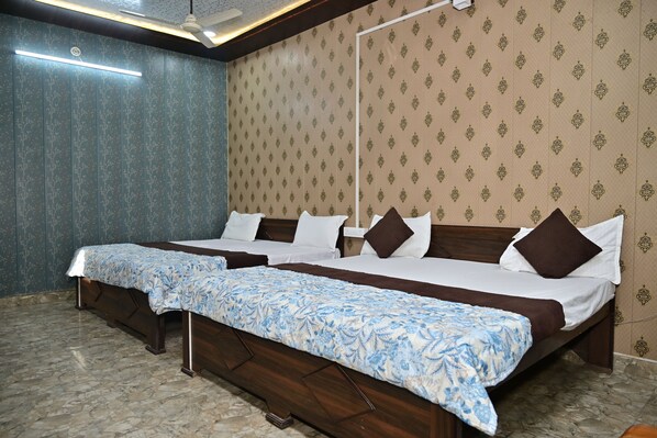 A hotel room with two beds, a ceiling fan, a wall-mounted light, and patterned wallpaper. - Anamika Palace (Faizabad)