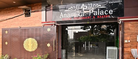 Un restaurante y panadería con fachada moderna, entrada de vidrio y plantas en macetas decorativas afuera.