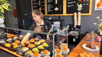 A bakery counter with various pastries and desserts displayed in clear containers, a menu board above, and a coffee machine to the side.
