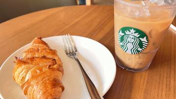 A croissant on a white plate with a fork beside it, and a Starbucks iced coffee cup with a straw.