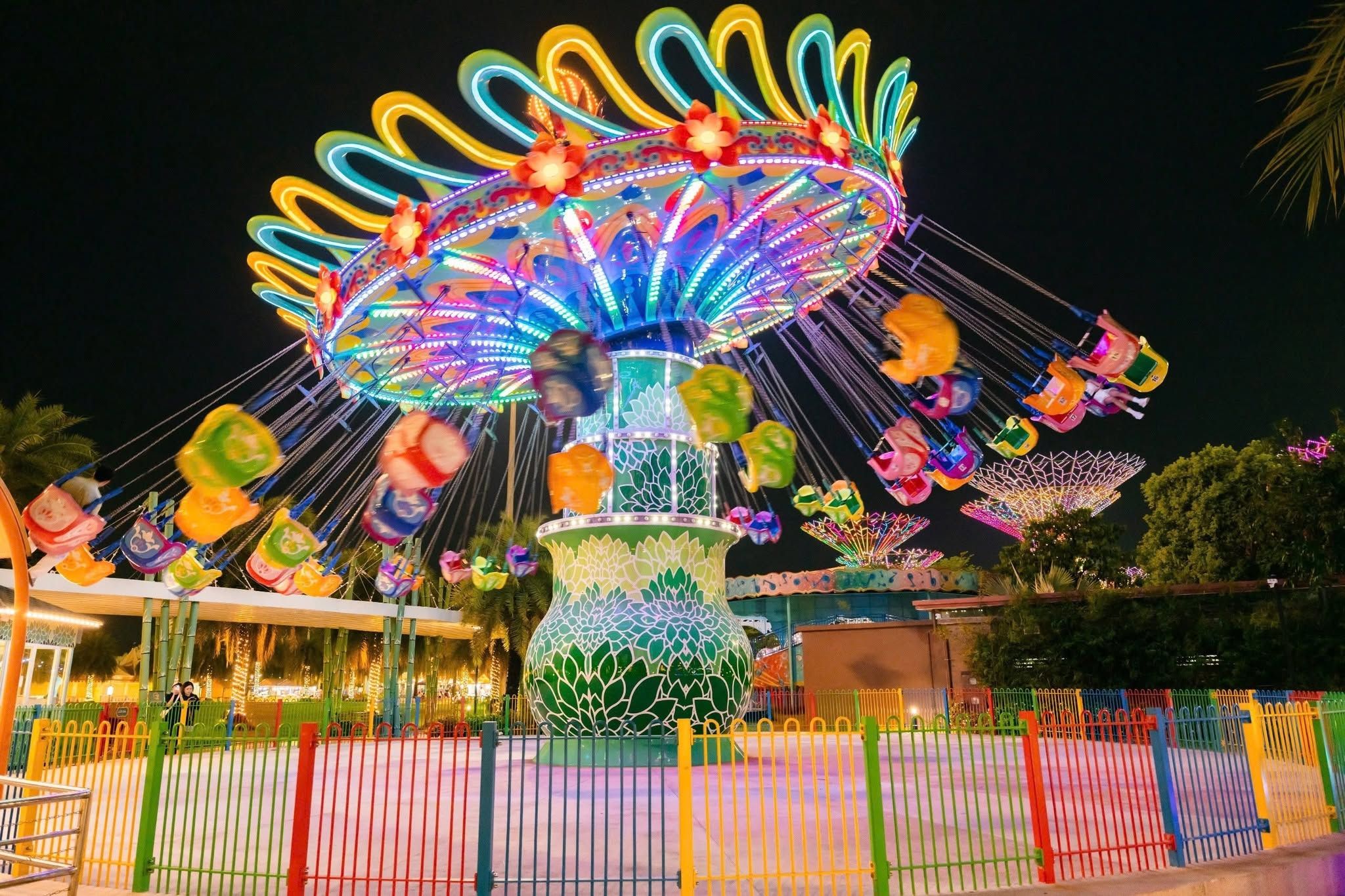 A brightly lit amusement ride with a floral design and colorful seats.