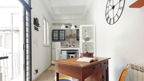 A room with a wooden table, a chair, a clock on the wall, and a kitchen area in the background. - Secret refuge in the heart of Rome (Roma)