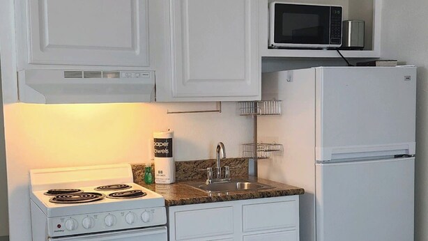 A kitchen with white cabinets, a stove, a microwave, and a refrigerator.