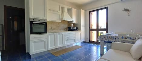 A compact kitchen with white cabinets, a built-in oven, and a dining area with a table and chairs.