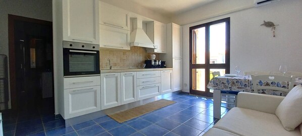 A compact kitchen with white cabinets, a built-in oven, and a dining area with a table and chairs.