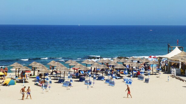 Een strand met veel parasols en ligbedden, een zandstrand en de oceaan op de achtergrond.