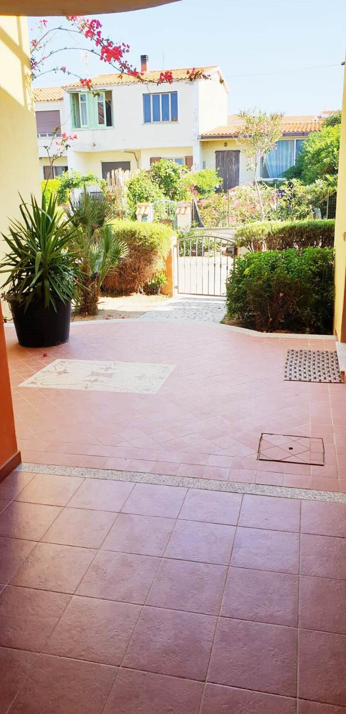 A courtyard with tiled flooring, potted plants, and a gated entrance leading to a building with a tiled roof.