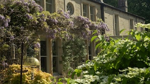 A historic stone building with large windows and a garden with purple flowers and greenery. - Outwood House (Leeds)