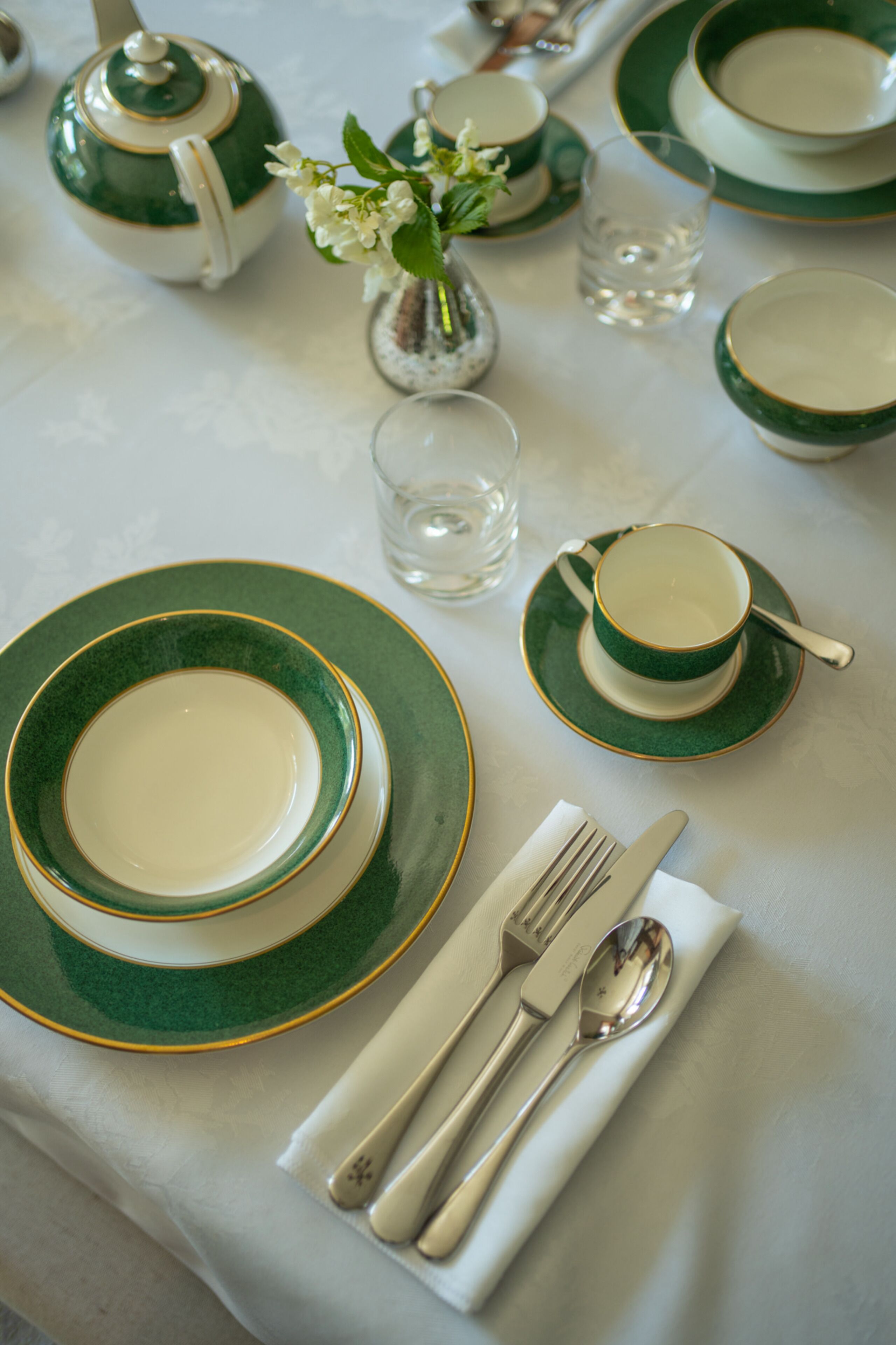 A table set with green and white plates, bowls, a teapot, and silverware.