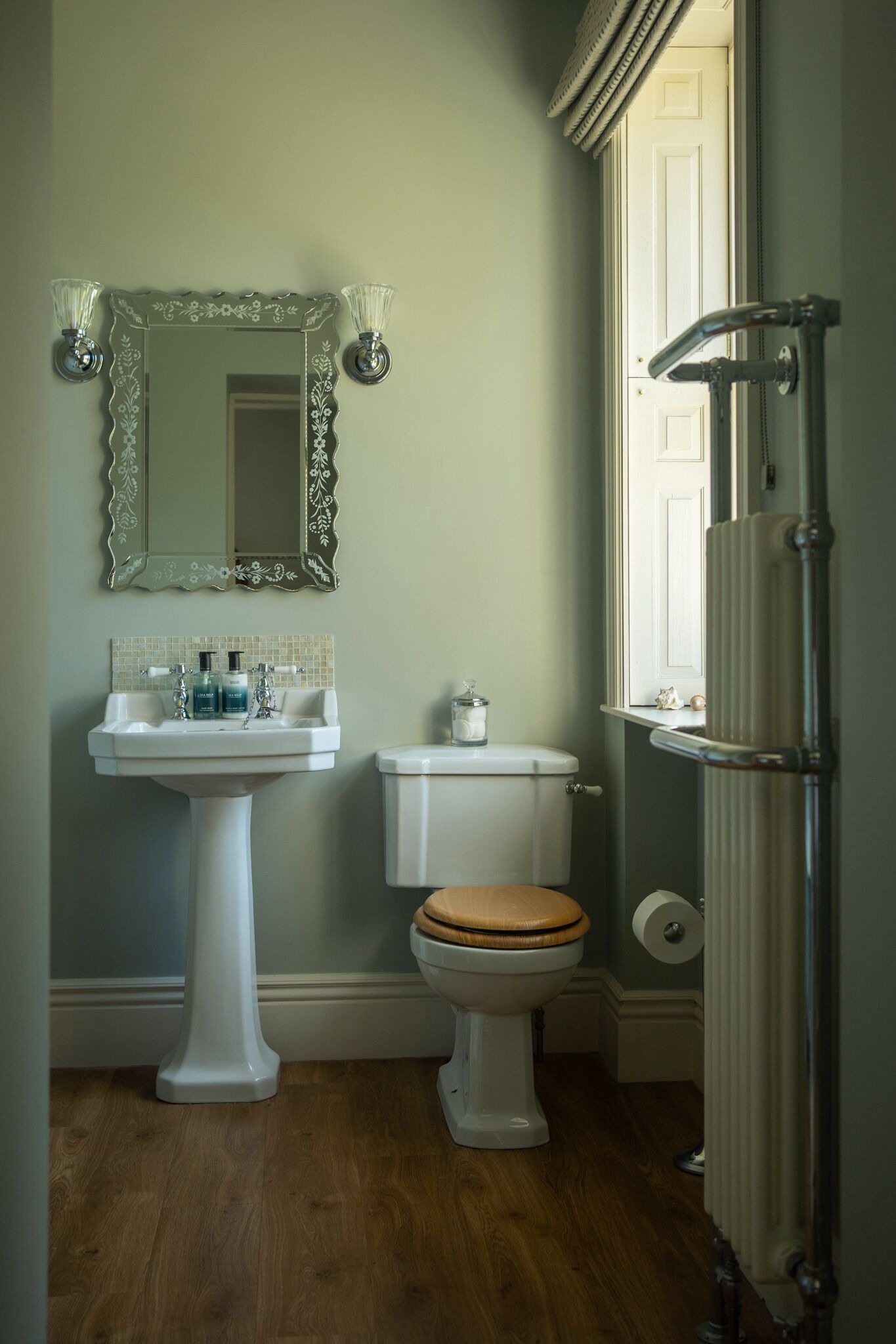 Un baño con lavamanos pedestal, inodoro y ducha con mampara de vidrio.
