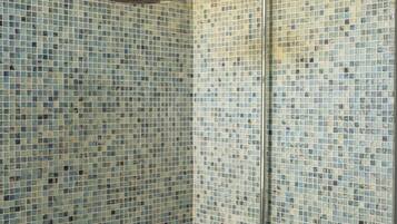 A shower with a mosaic tile wall and a chrome showerhead.