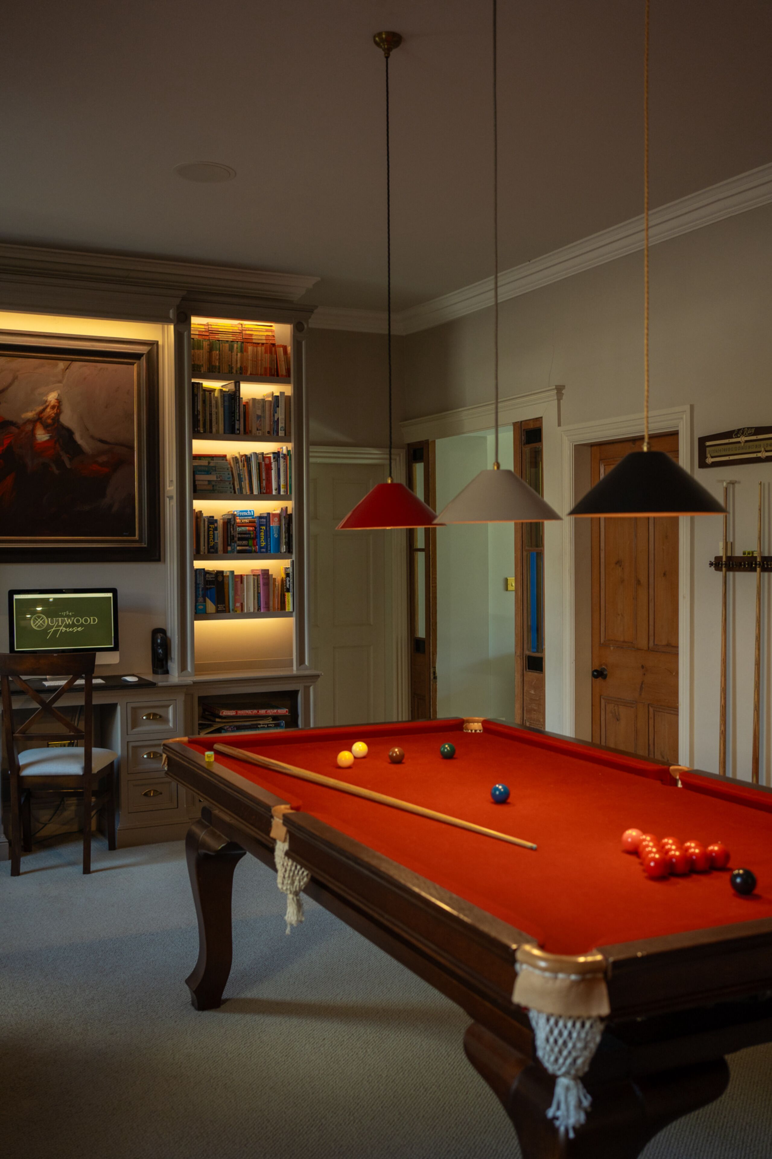 A billiards table with balls, a bookshelf, and a painting on the wall.