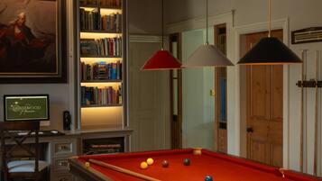 A billiards table with balls, a bookshelf, and a painting on the wall.