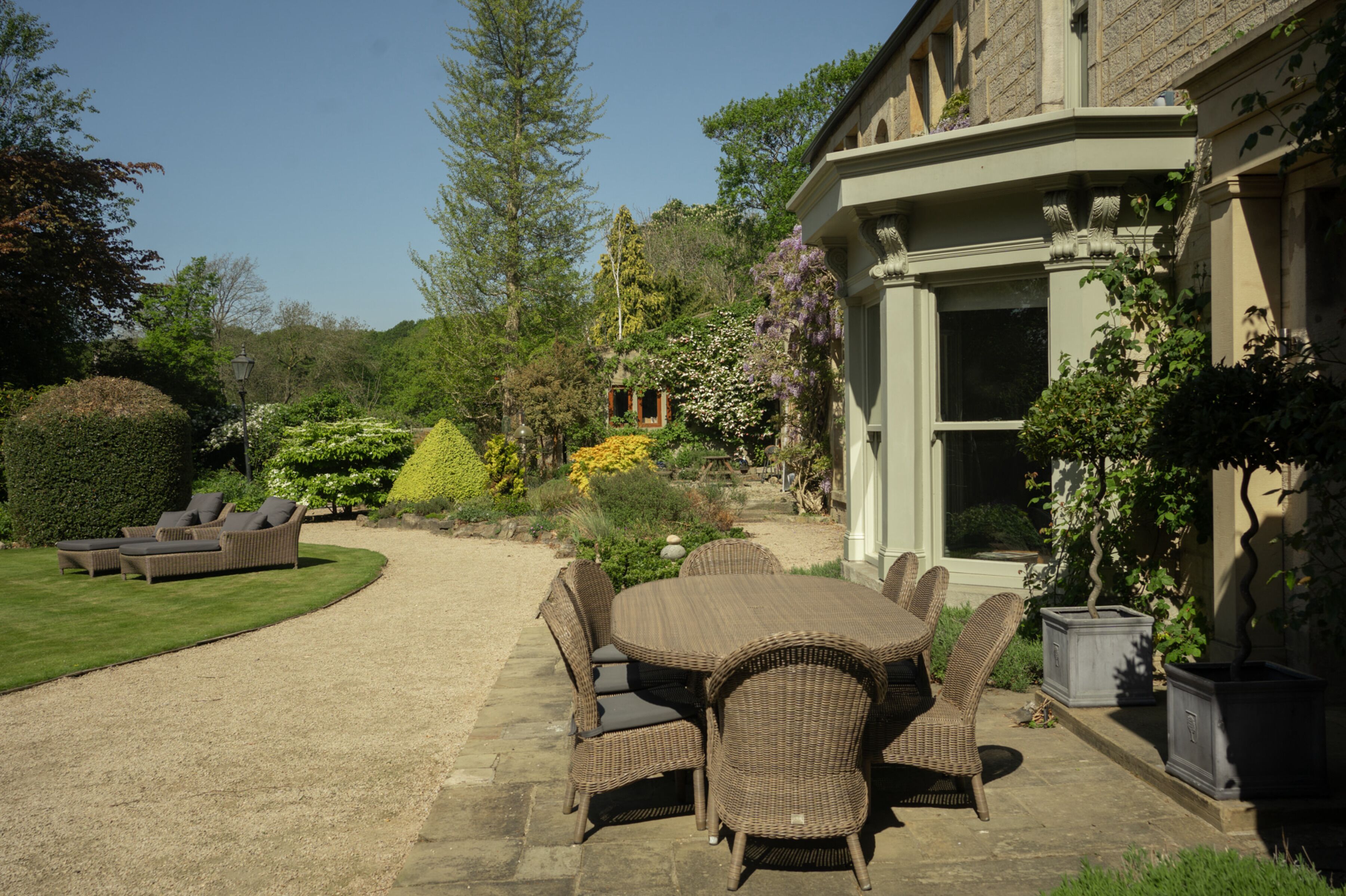 A patio with wicker furniture, a stone pathway, and a garden with various plants and a building in the background.