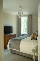 A bedroom with a bed, a television on a wooden dresser, a chandelier, and a window with curtains.