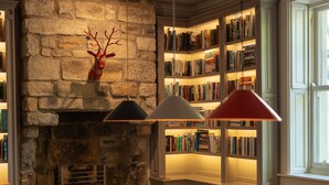 A pool table with balls, a fireplace, and bookshelves in a room with a stone wall and a window. - Outwood House (Leeds)