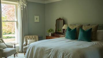 Quarto com cama grande, uma cadeira, cômoda, espelho e janela com cortinas.