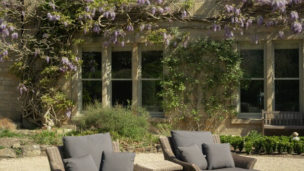 A stone building with large windows and a garden with two wicker lounge chairs. - Outwood House (Leeds)