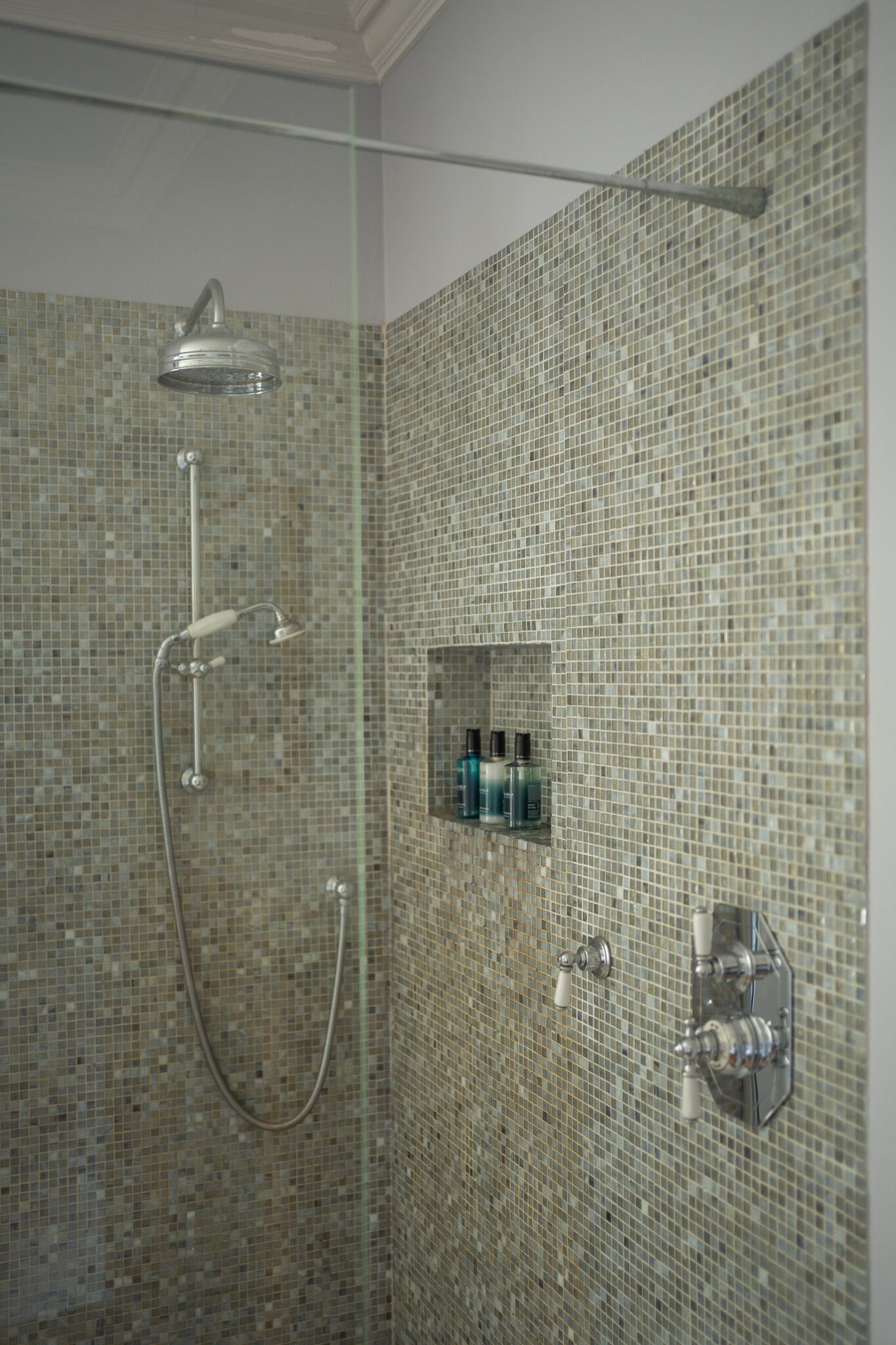 Eine Dusche mit Glastür, Handbrause und am Wand montiertem Wasserhahn.