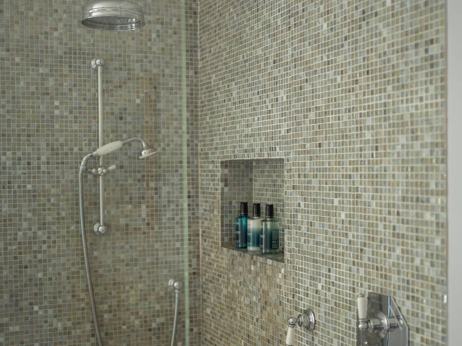 Eine Dusche mit Glastür, Handbrause und am Wand montiertem Wasserhahn.