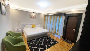A bedroom with a bed, green armchair, wooden floor, and a black and white rug. - BRIKitt Himaliyan Vista 2BHK - Mukteshwar, Nainital (Mukteshwar)
