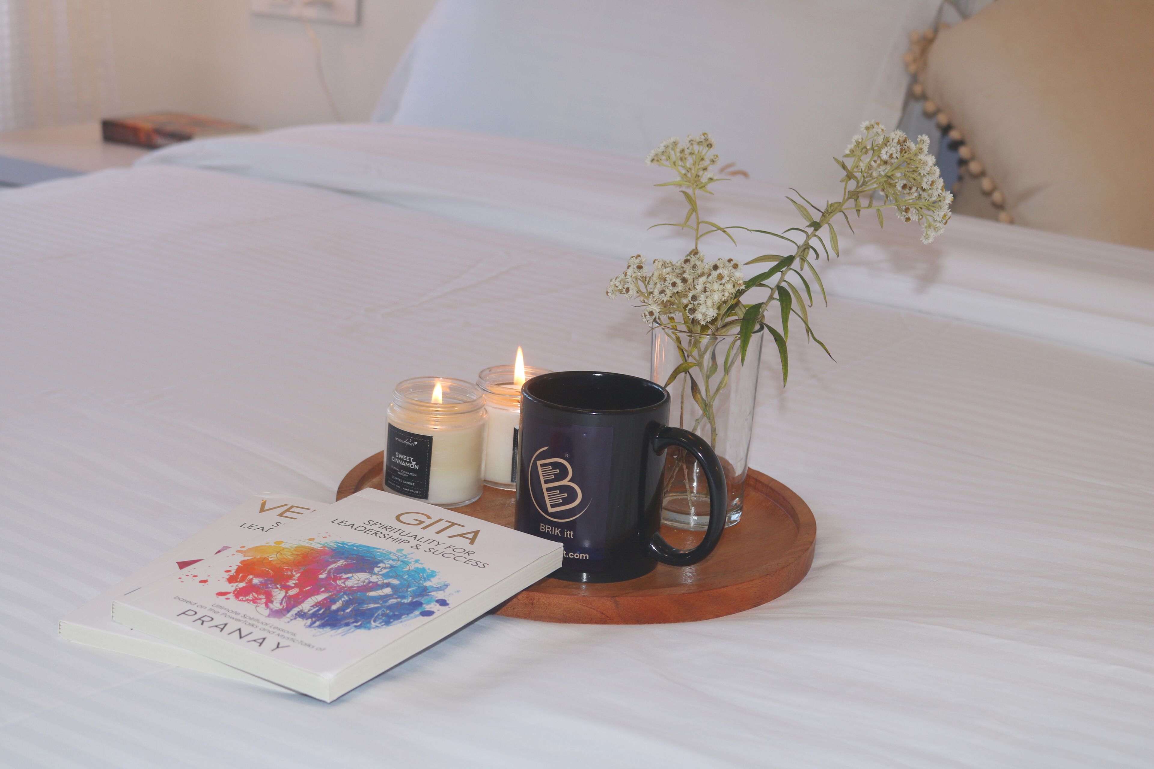 A neatly made bed with a book, a mug, and candles on a tray.