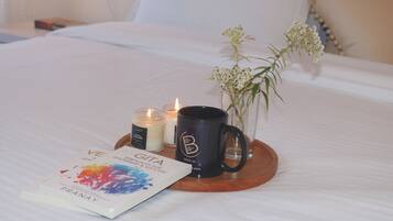 A neatly made bed with a book, a mug, and candles on a tray.