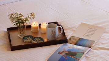 A tray with candles, a mug, and a small vase with flowers on a bed.