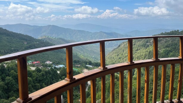 A wooden balcony railing overlooking a mountainous landscape with scattered houses. - BRIKitt Himaliyan Vista 2BHK - Mukteshwar, Nainital (Mukteshwar)
