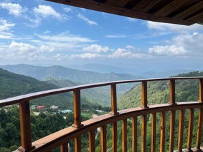 Barandilla de madera de un balcón con vistas a un paisaje montañoso salpicado de casas.