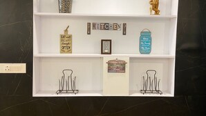 A kitchen shelf with decorative items including a plant, a golden figurine, a sign saying "EAT well LIVE simply laugh often," a jar with a message, and two wire racks. - BRIKitt Himaliyan Vista 2BHK - Mukteshwar, Nainital (Mukteshwar)